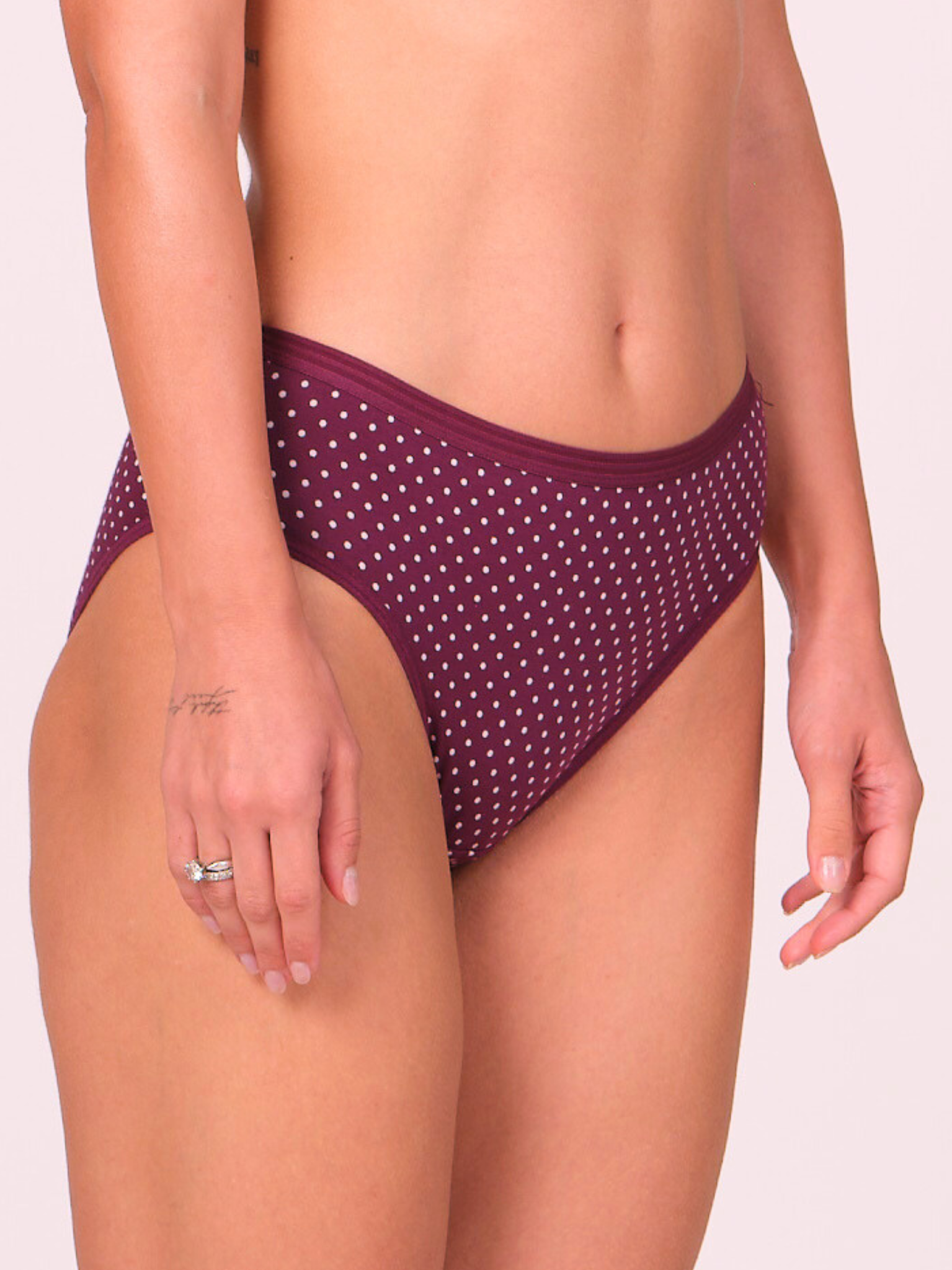Purple polka dot bikini bottom worn by a person on a light pink background