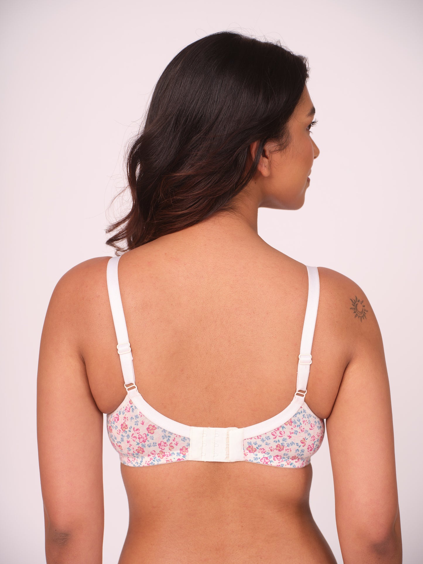 Woman wearing a white floral bra against a plain background